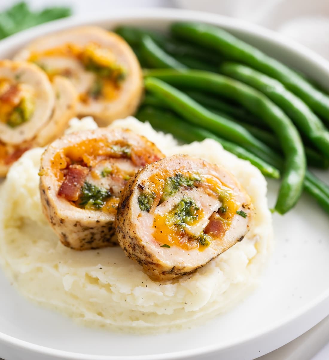 Slices of Chicken Roulade on top of mashed potatoes with green beans in the background.