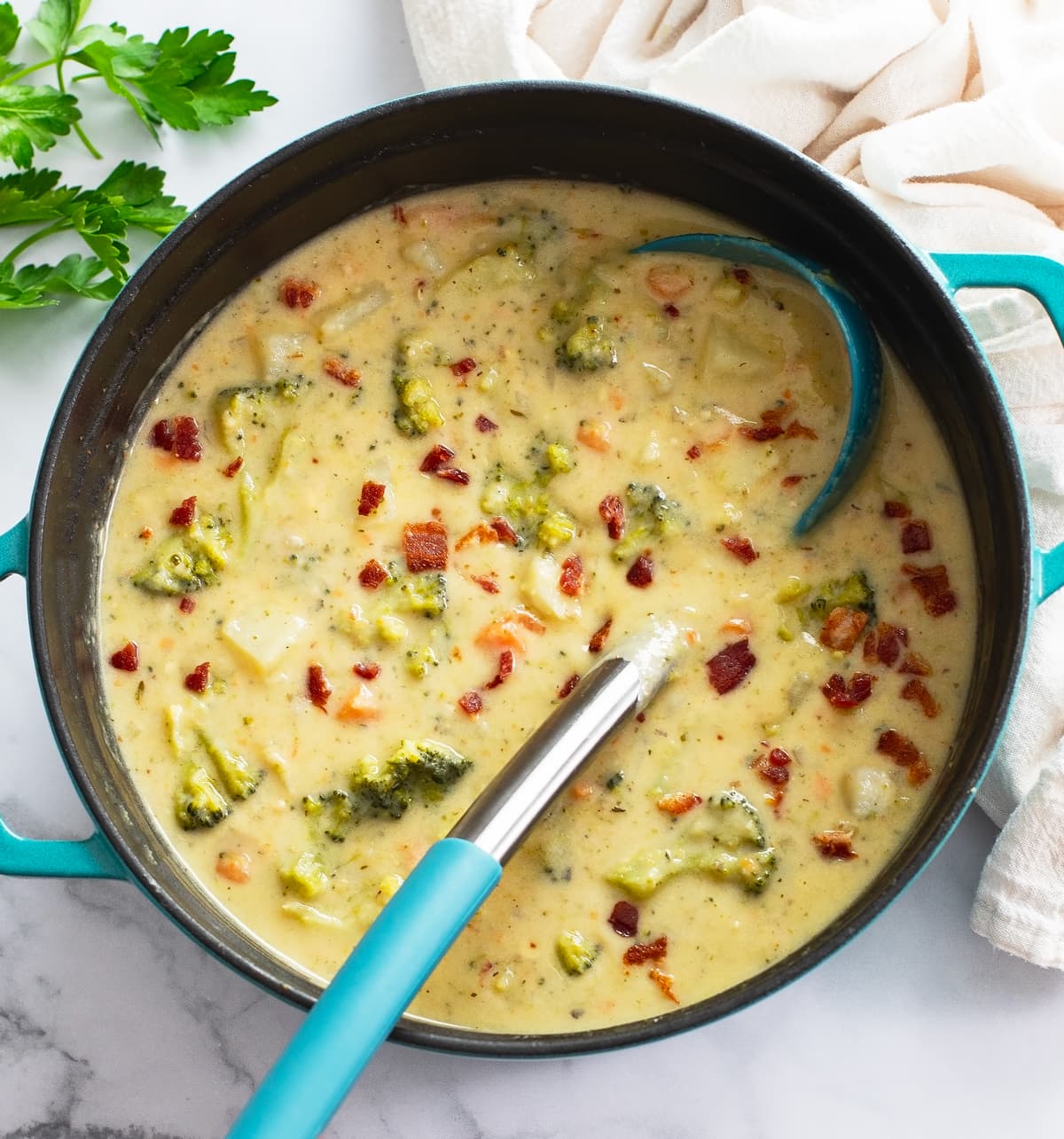 A soup pot of Broccoli Potato Soup with bacon on top and a ladle on the side.