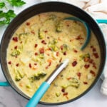 A pot of Broccoli Potato Soup with a soup ladle and bacon on top.