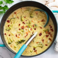 A pot of Broccoli Potato Soup with a soup ladle and bacon on top.