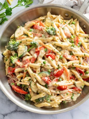 Pasta primavera in a skillet with a cream sauce and vegetables.