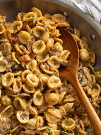 A wooden spoon scooping up French Onion Pasta from a skillet.
