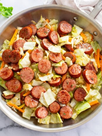 Cabbage and Sausage in a skillet with slices of carrots and parsley.