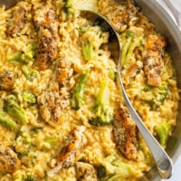 Chicken and Orzo in a skillet with broccoli and a creamy cheese sauce with a spoon on the side.