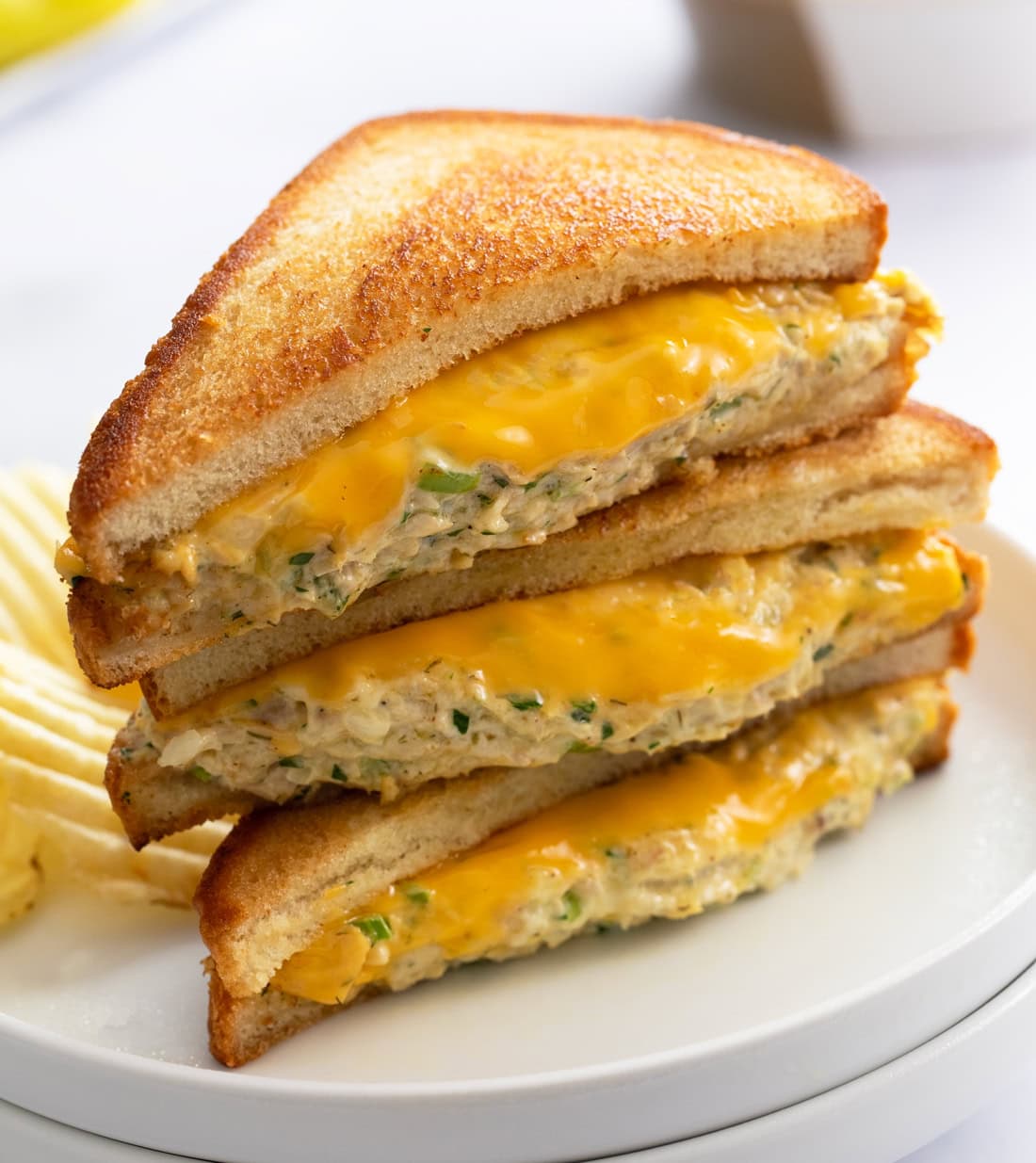 Slices of Tuna Melts stacked on top of each other on a white plate with melted cheese and grilled bread.