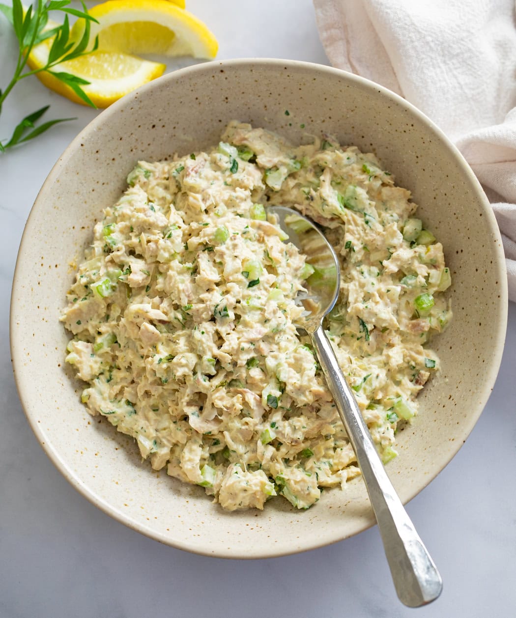 A bowl filled with Tuna Salad with a spoon on the side.