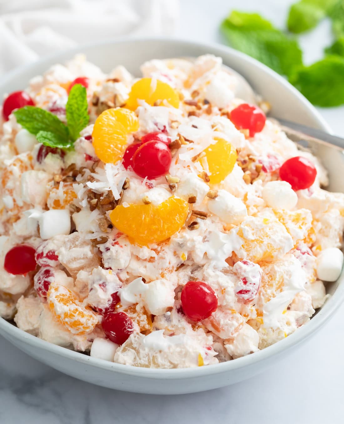Creamy Ambrosia Salad in a white bowl with cherries and mandarin oranges on top.