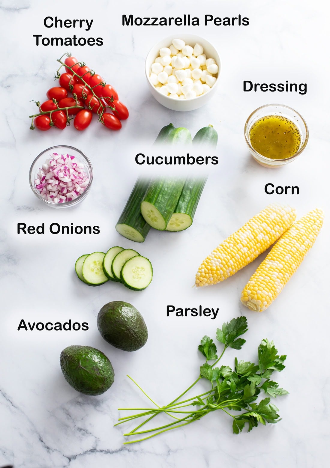 Labeled ingredients for making Cucumber Avocado Salad on a white surface.