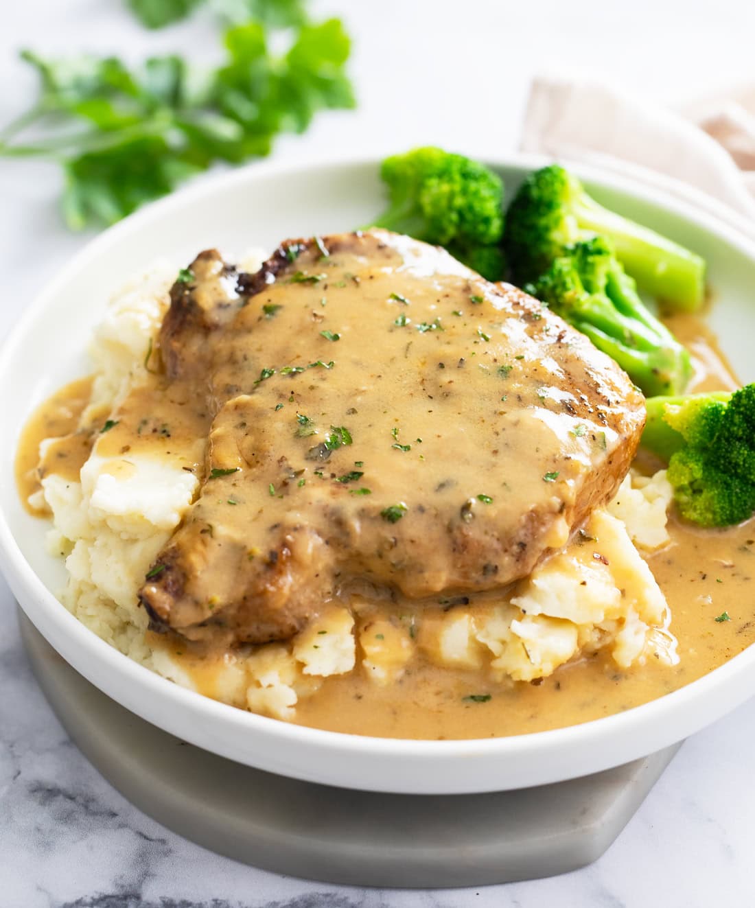 A Parmesan Garlic Pork Chop on top of mashed potatoes on a white plate with broccoli in the background.