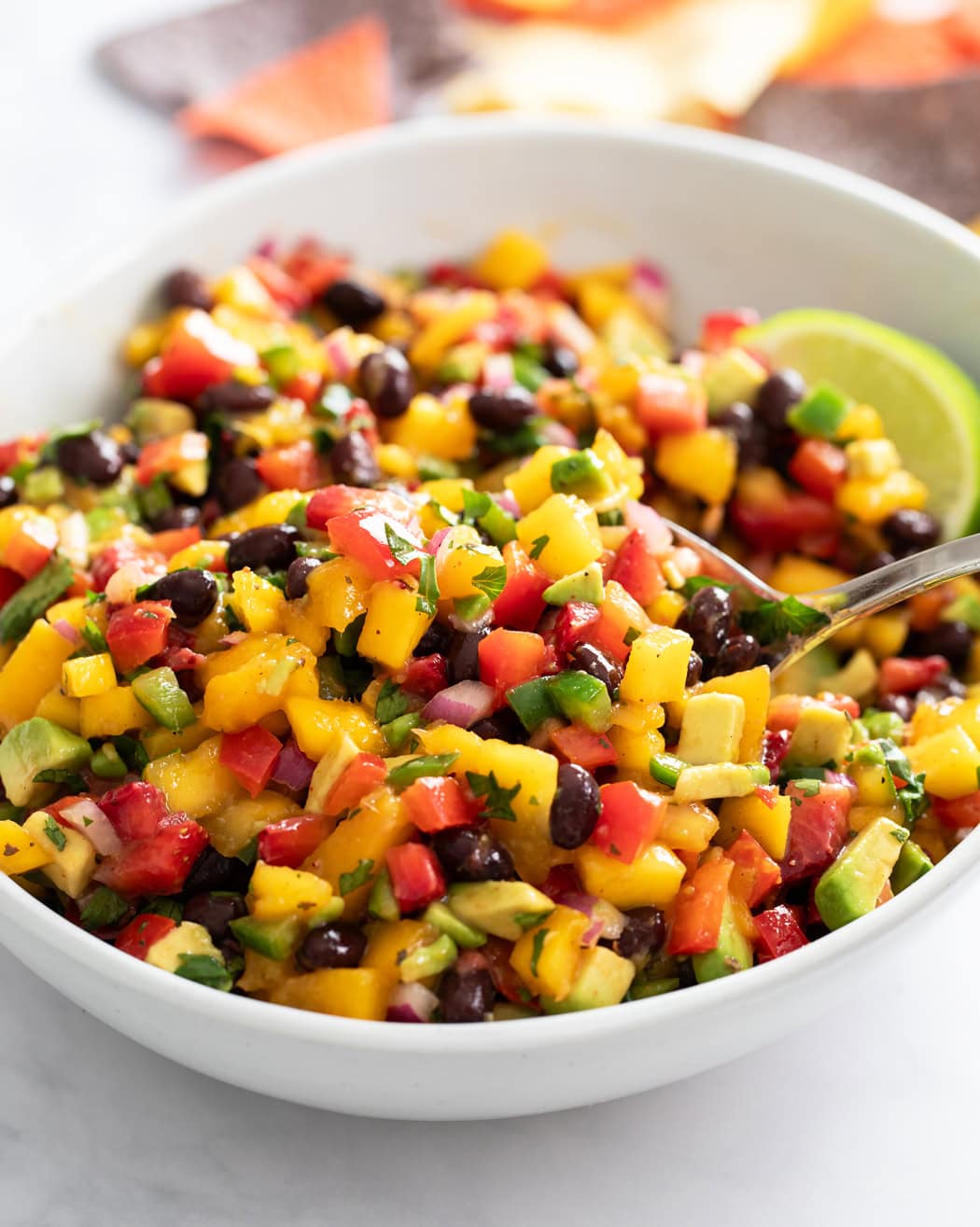Mango Salsa in a white bowl with a spoon scooping it up.