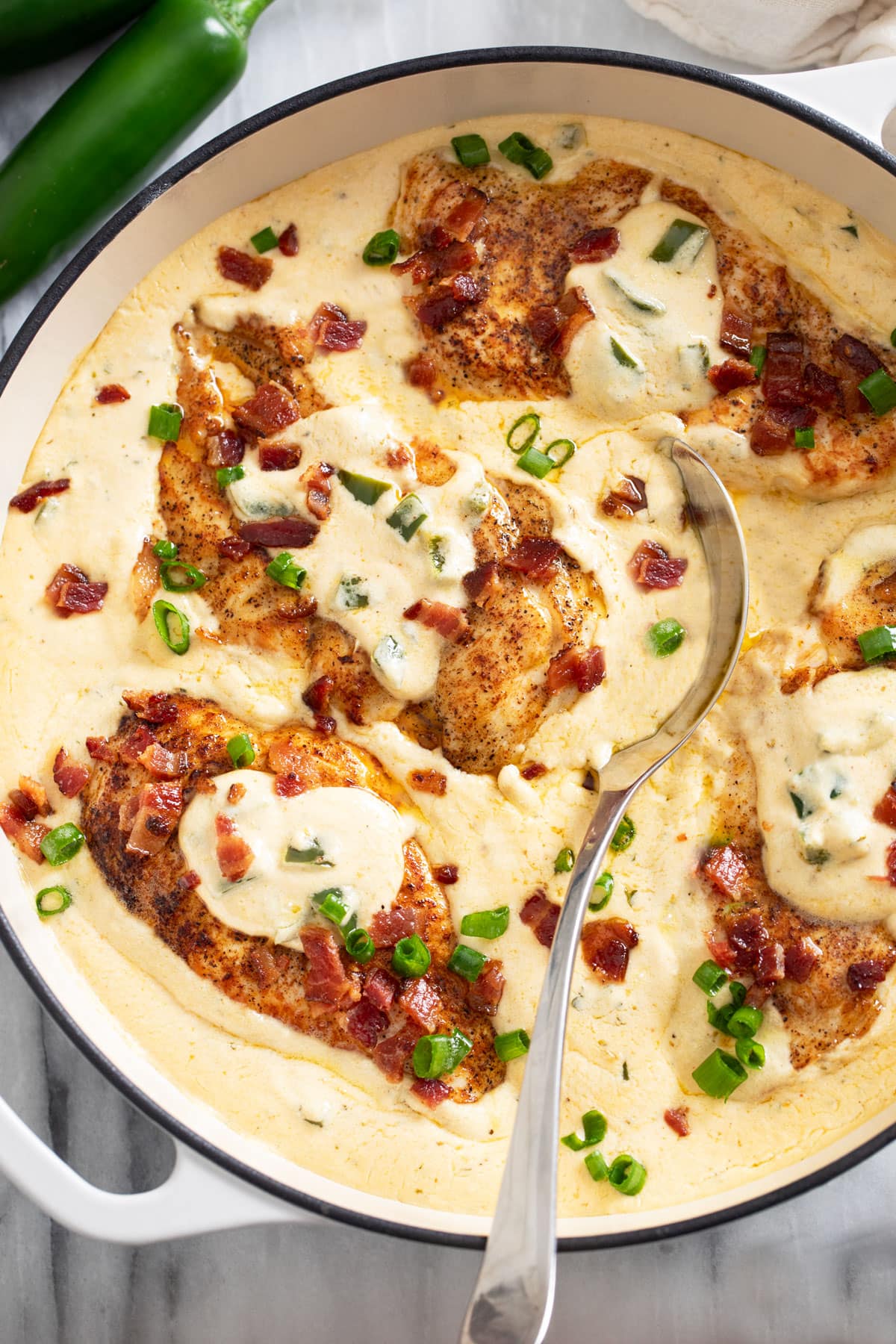 A skillet filled with Jalapeno Popper Chicken in a cream sauce with bacon and green onions.