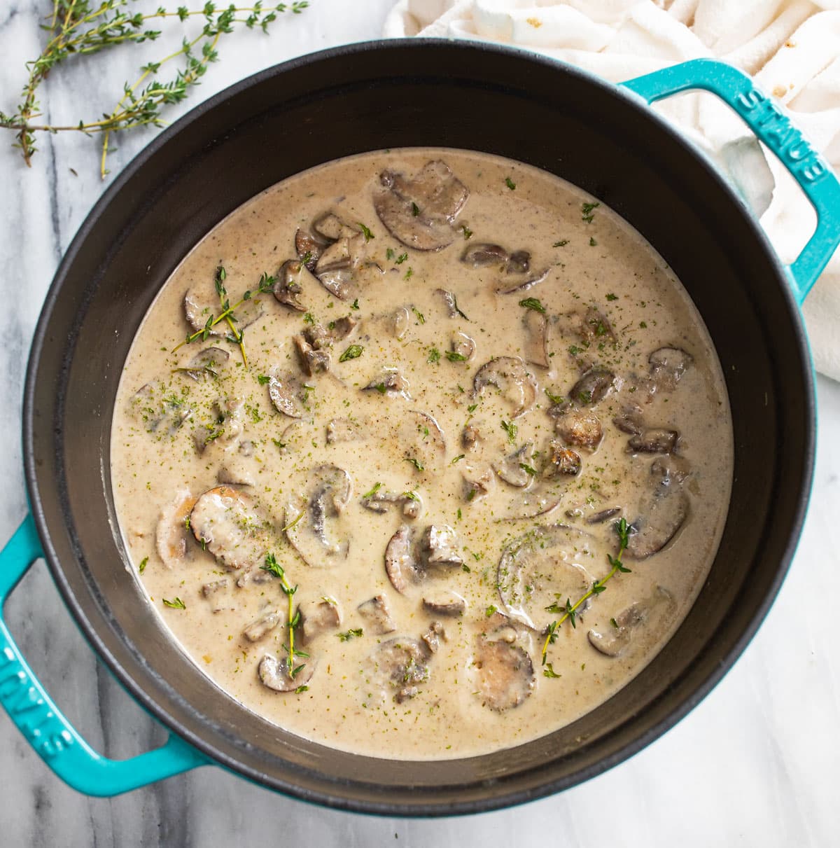A soup pot filled with Cream of Mushroom Soup with fresh thyme on top.