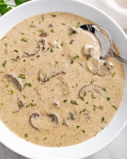 Cream of Mushroom Soup in a white bowl with a spoon on the side and parsley on top.