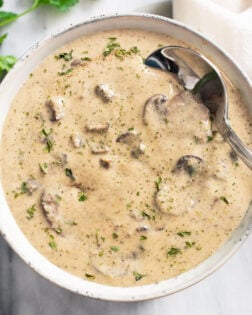 Cream of mushroom soup in a white bowl with parsley on top and a spoon on the side.
