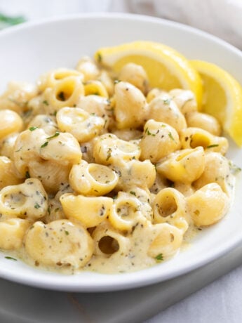 Garlic Butter Pasta on a white plate with lemon slices in the background.