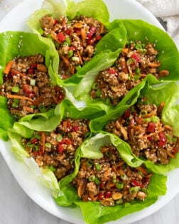 Chicken Lettuce Wraps on a white platter with toppings and chicken in sauce.