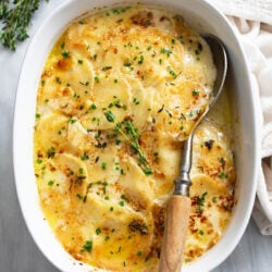Cheesy Au Gratin Potatoes in a cream sauce with chives on top and a serving spoon on the side.