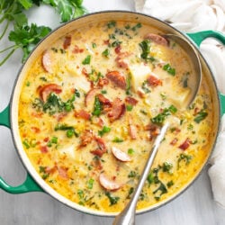 Kielbasa Potato Soup in a soup pot with bacon and green onions on top and a ladle on the side.