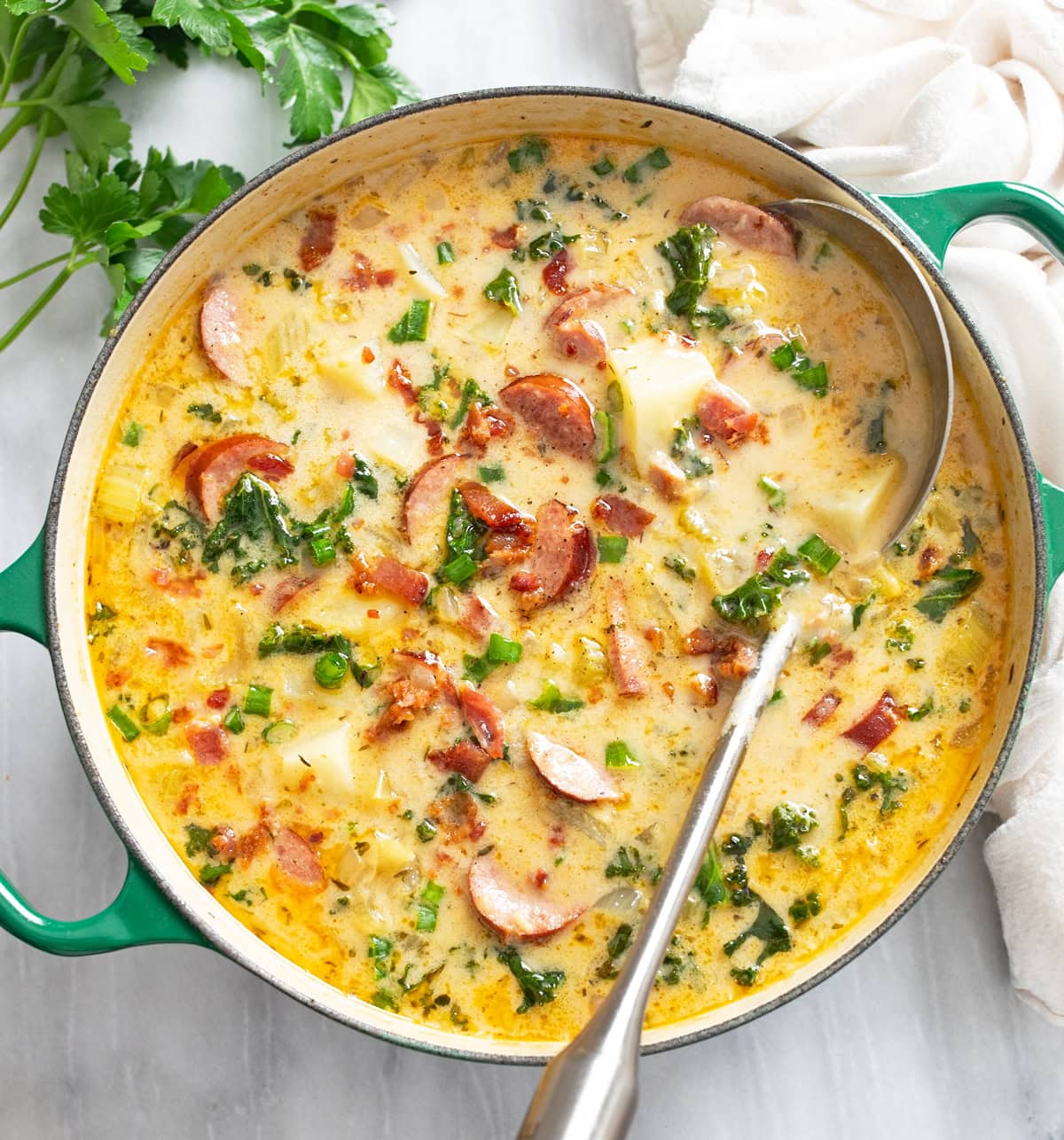 Kielbasa Potato Soup in a green soup pot with a ladle on the side.