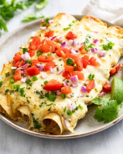 Cheesy White Chicken Enchiladas on a plate with lime wedges and cilantro on the side.