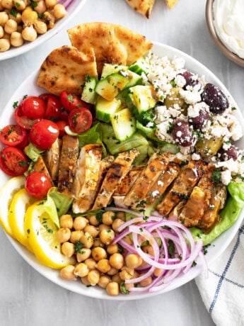 Overhead view of Greek Chicken Bowls in a white bowl with vegetables, olives, feta, and chickpeas.