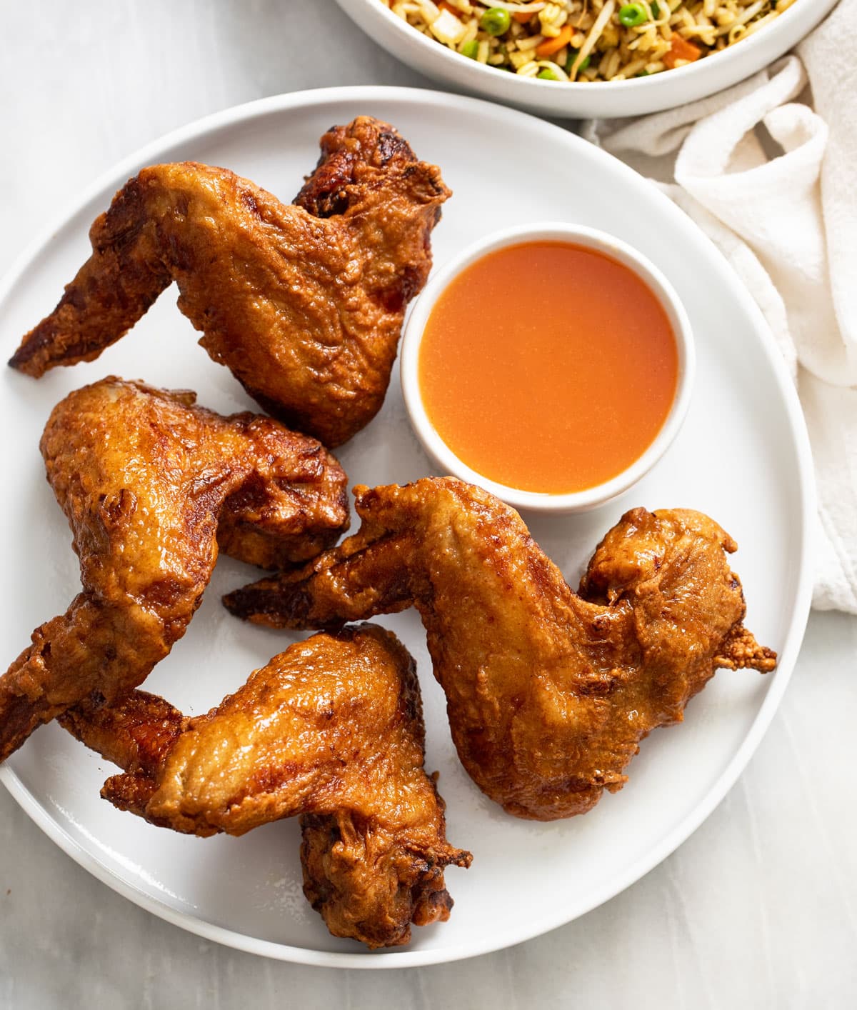 Fried Chinese Chicken Wings on a white plate with sweet and sour sauce on the side.
