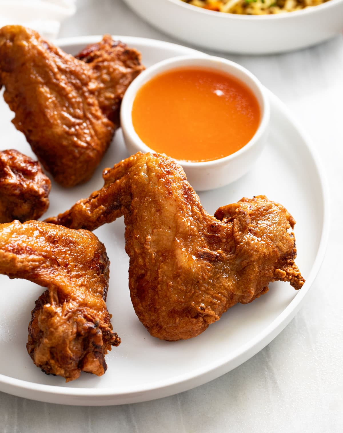 A side view of a Chinese Chicken Wing on a white plate with sweet and sour sauce in the back.
