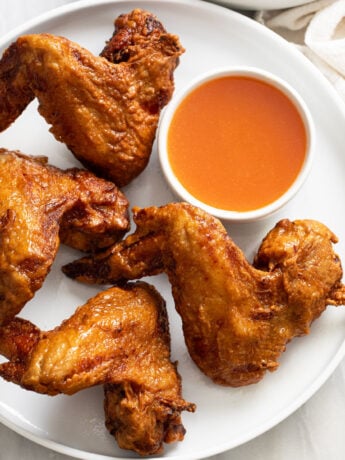 Fried Chinese Chicken Wings on a white plate with sweet and sour sauce on the side.