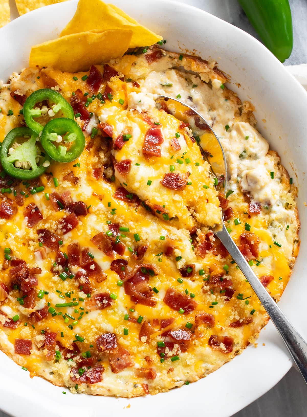 A spoon scooping up Jalapeno Popper Dip from a baking dish.