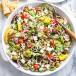 Greek Salad in a white bowl with vegetables, chickpeas, dressing, and feta.