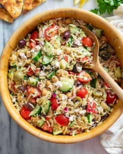Orzo Salad in a wooden bowl with a spoon on the side.