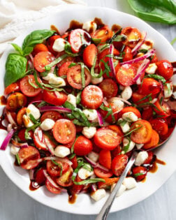 Tomato Salad in a white bowl with fresh basil, mozzarella, red onions, and balsamic glaze.