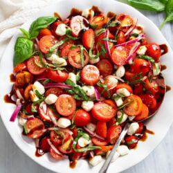 Tomato Salad in a white bowl with mozzarella pearls, fresh basil, red onions, and homemade balsamic dressing.