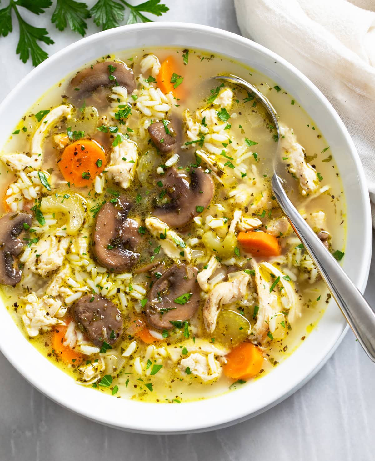 A white bowl of chicken and mushroom soup with rice in it and a spoon on the side.