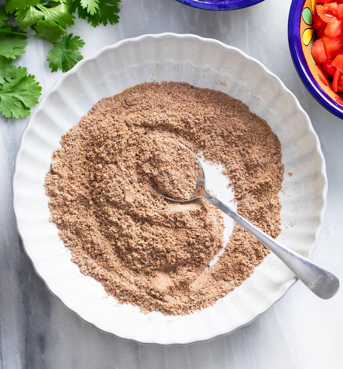 Combined Taco Seasonings in a white bowl after being mixed together with a spoon on the side.
