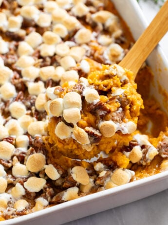 A wooden spoon scooping Sweet Potato Casserole from a white casserole dish.