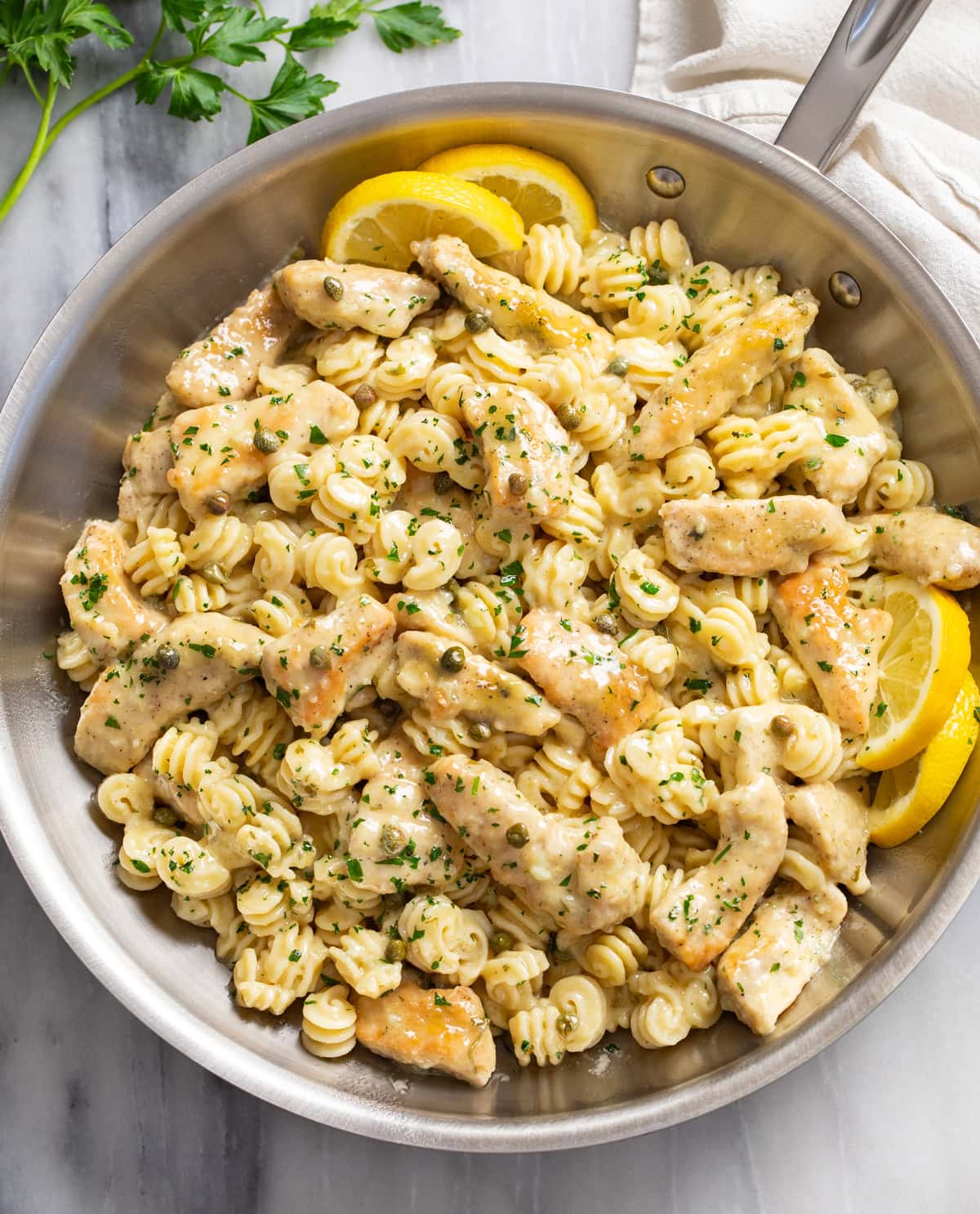 Chicken Piccata Pasta in a skillet with lemon wedges and fresh parsley.