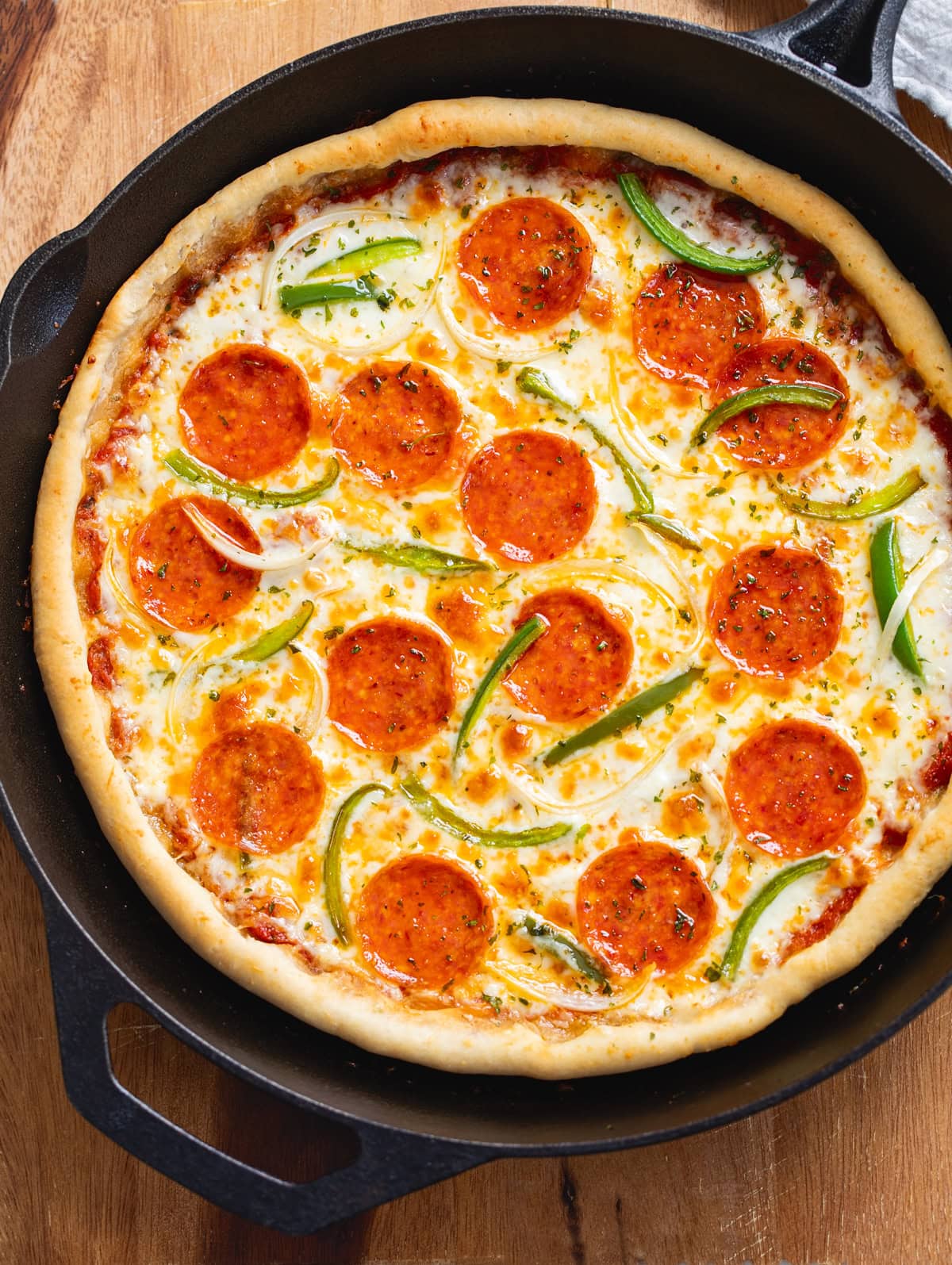 Pizza in a cast iron skillet topped with pepperoni, onions, and peppers.