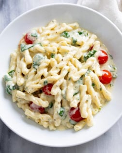 A white plate filled with Boursin pasta with a creamy herb sauce, tomatoes, and spinach.