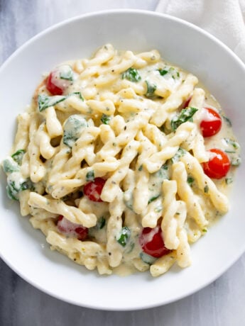 A white plate filled with Boursin pasta with a creamy herb sauce, tomatoes, and spinach.