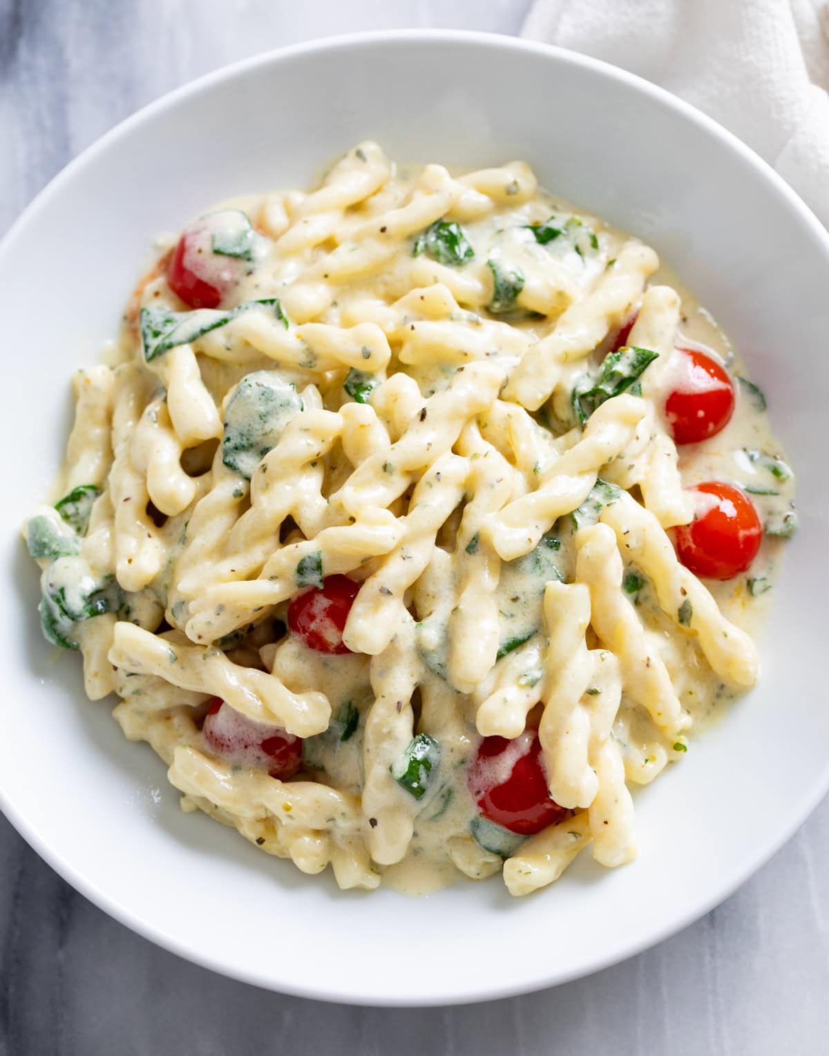 A white plate filled with Boursin pasta with a creamy herb sauce, tomatoes, and spinach.