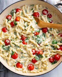 Boursin Pasta with a creamy herb sauce, spinach, and tomatoes in a skillet with a wooden spoon on the side.