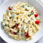 Creamy Boursin Pasta with an herb cream sauce, spinach, and tomatoes in a white bowl.