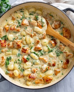 Creamy Chicken Gnocchi in a skillet with seared chicken and a creamy sauce with spinach and a wooden spoon on the side.