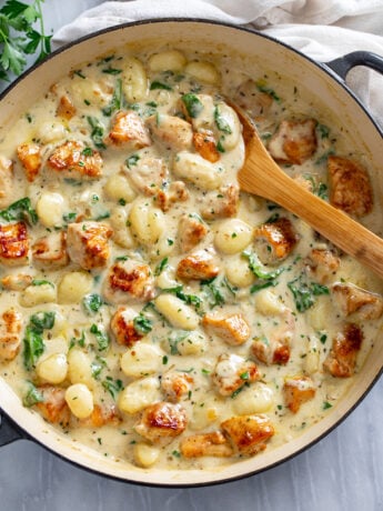 Creamy Chicken Gnocchi in a skillet with seared chicken and a creamy sauce with spinach and a wooden spoon on the side.