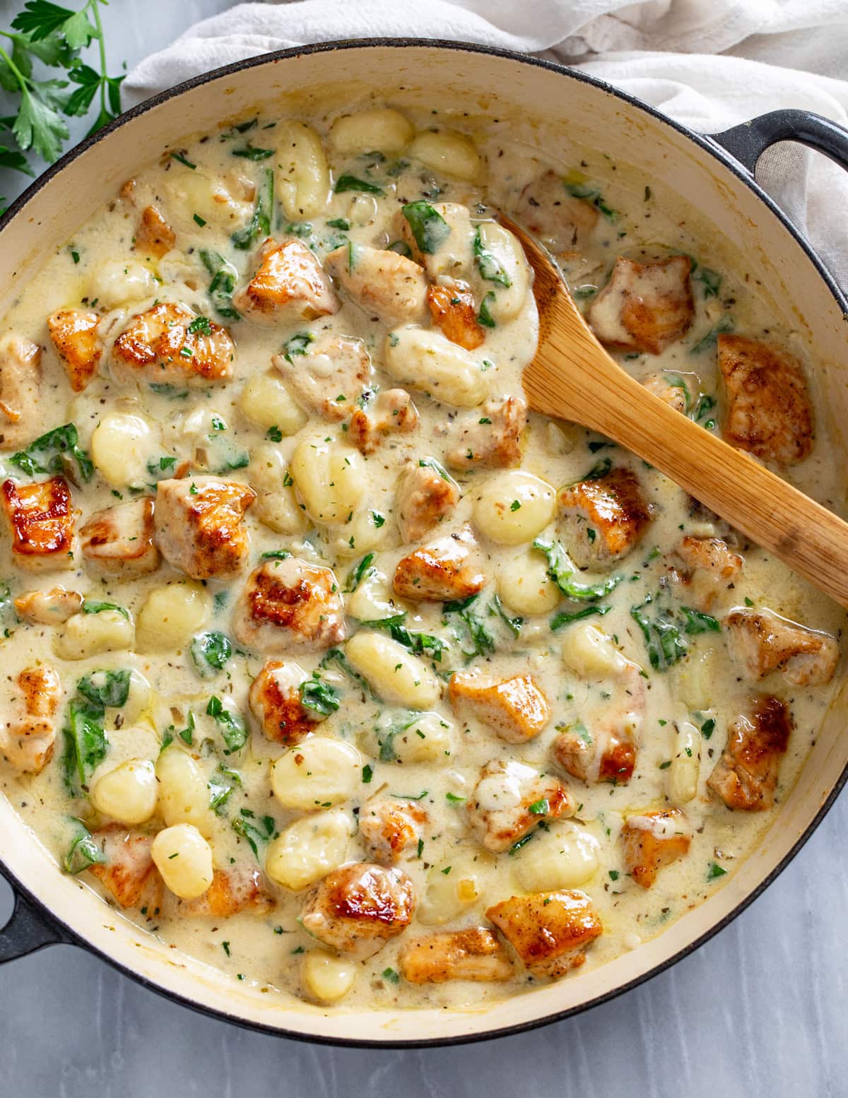 Creamy Chicken Gnocchi in a skillet with seared chicken and a creamy sauce with spinach and a wooden spoon on the side.
