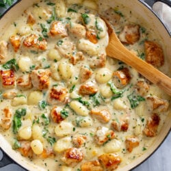 A skillet filled with Creamy Chicken Gnocchi with spinach and a wooden spoon on side.