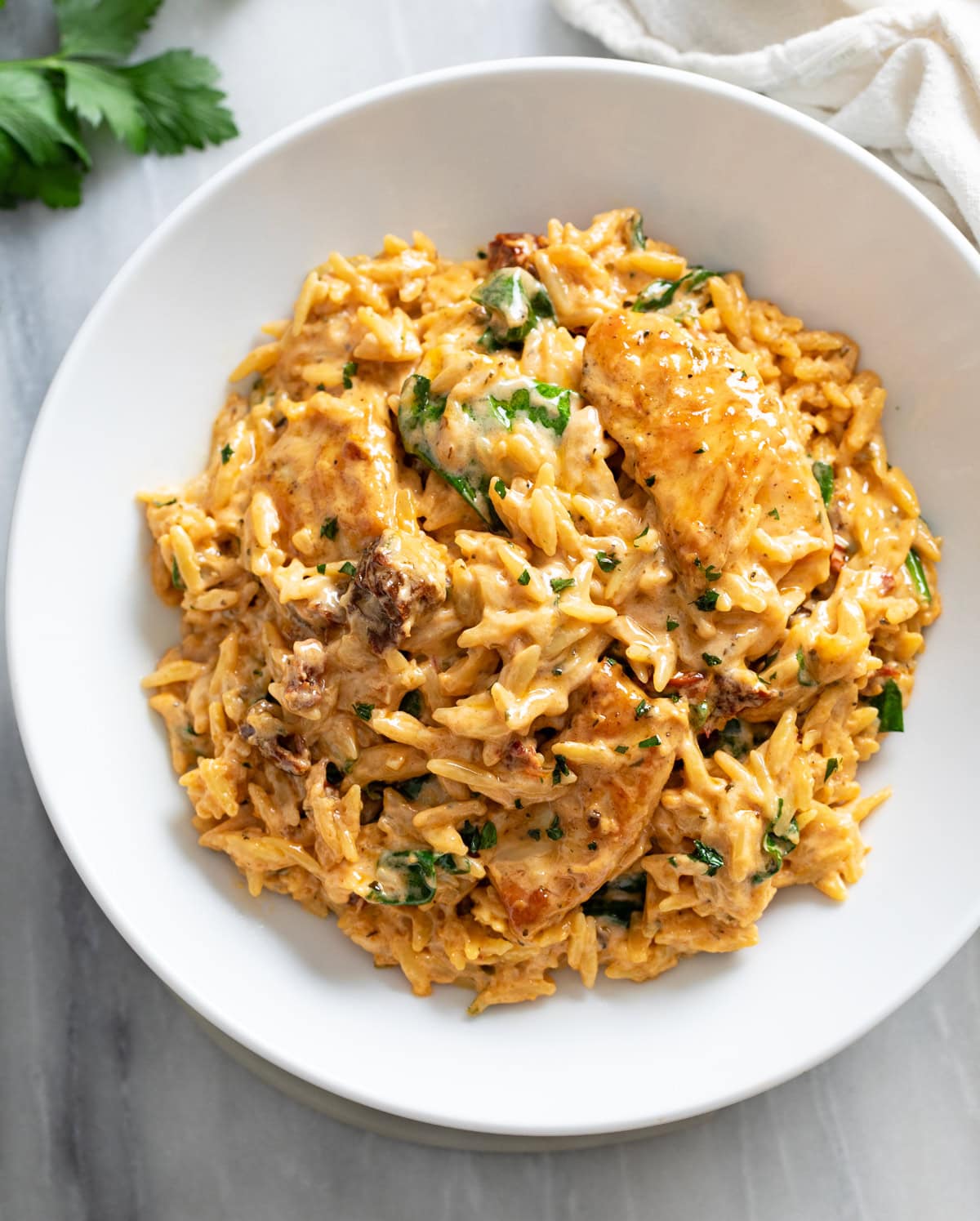 A white bowl filled with Marry Me Chicken Orzo in a tomato cream sauce with sun-dried tomatoes and spinach.