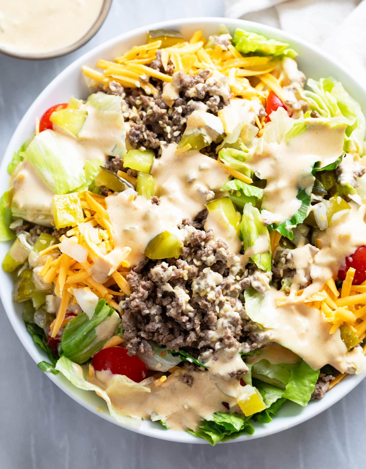 A white bowl filled with Big Mac Salad with Big Mac Sauce drizzled on top.