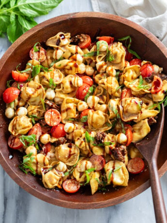 Caprese Pasta Salad in a wooden bowl with balsamic glaze drizzled on top.